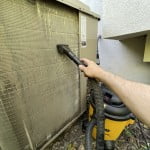 Shop vac with brush attachment cleaning the surface of an AC outdoor condenser coils.