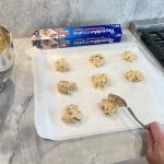 Chocolate chip cookie dough balls placed on parchment paper cookie sheets for baking.